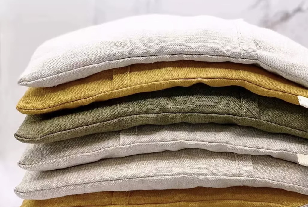 A stack of hand-filled linen eye pillows in oatmeal, mustard and olive colourways.